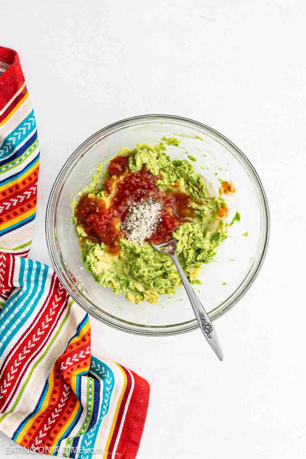 Smashed avocados in a bowl topped with salsa and spices.
