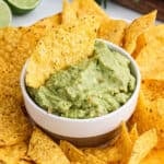 Guacamole in a dish with tortilla chips dipped into it.