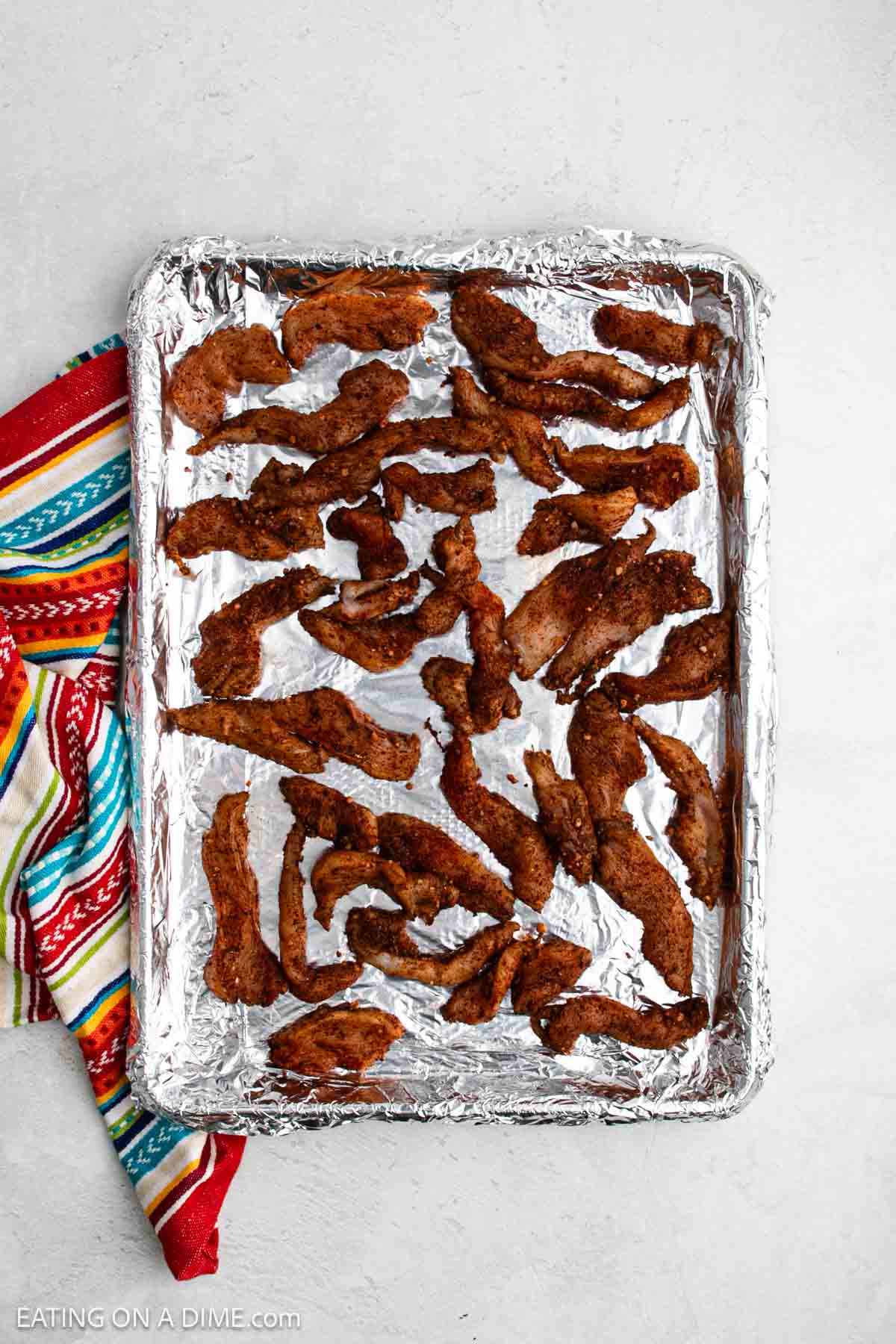 A foil-lined baking sheet with cooked, seasoned sheet pan chicken fajitas is spread out; a colorful striped cloth sits beside the pan on a light surface.
