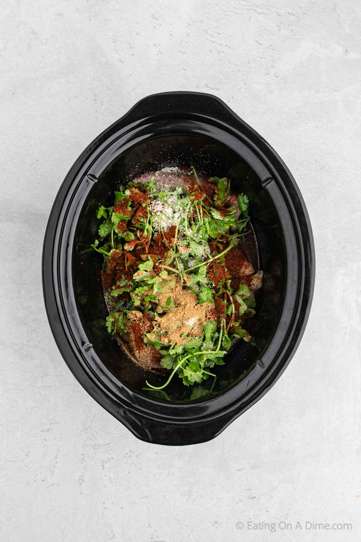 Topping the chicken with cilantro and seasoning in the slow cooker