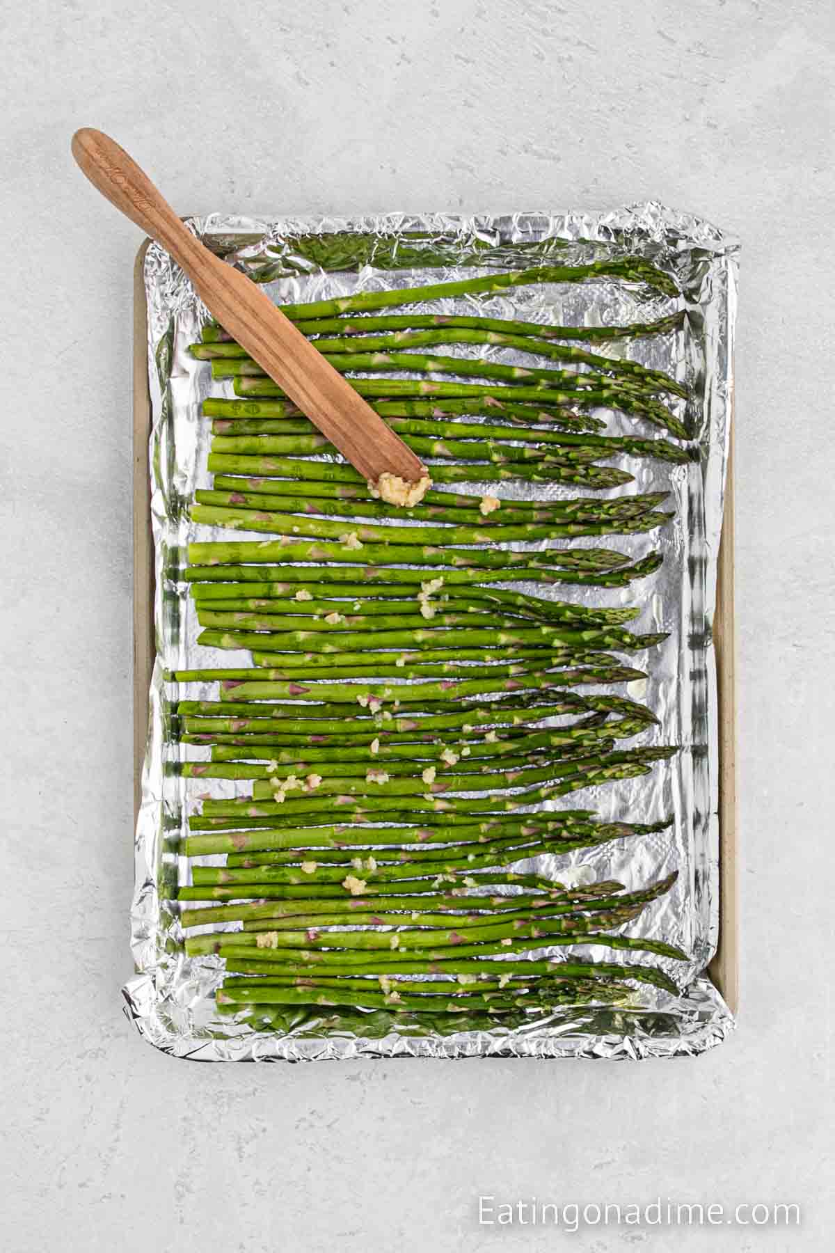 Topping the asparagus with minced garlic on the foil lined baking sheet