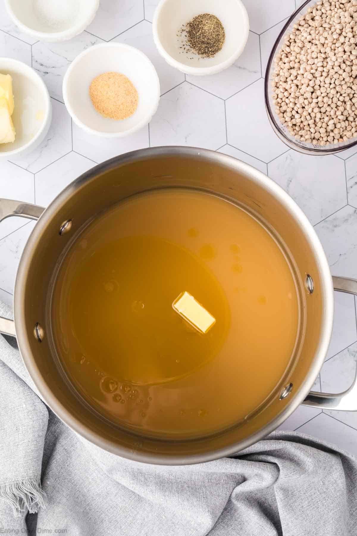 Adding the butter, broth, oil and seasoning to a large pot