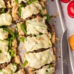Sliced Philly Cheesesteak Bread sandwiches with melted cheese, green bell peppers, and beef on bread, arranged on a baking sheet next to a knife.
