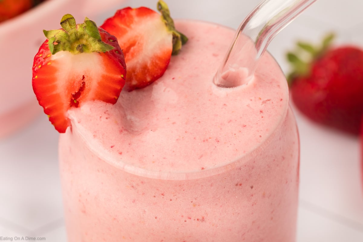 Strawberry Protein Shake in a glass with a straw and slice strawberries on the side