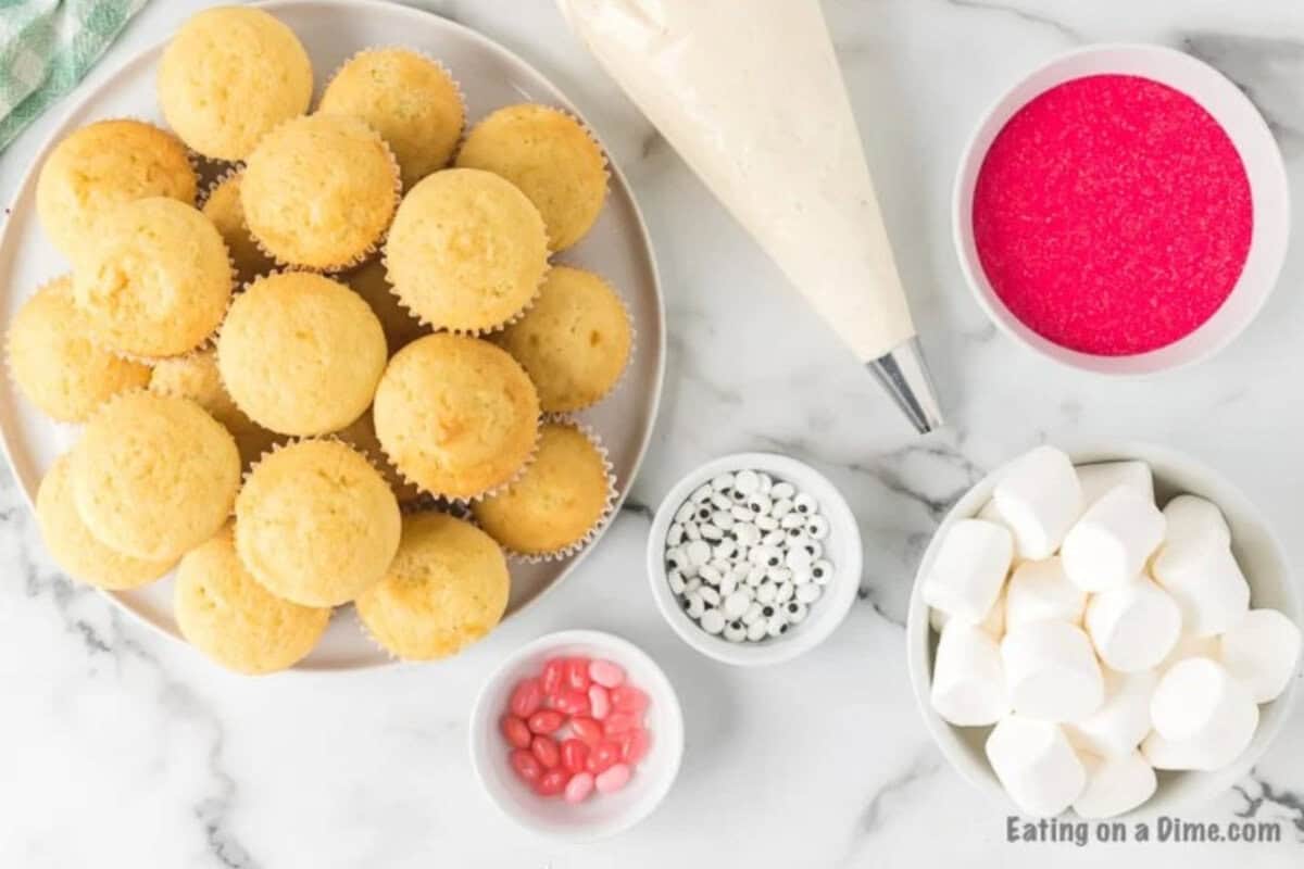 Easter to make bunny cupcakes in minutes! These quick and easy Easter Bunny Cupcakes are adorable but also taste great. Ingredients for recipe: baked cupcakes, bowl of pink sprinkles, jelly beans, candy eyes and large marshmallows in a bowl.