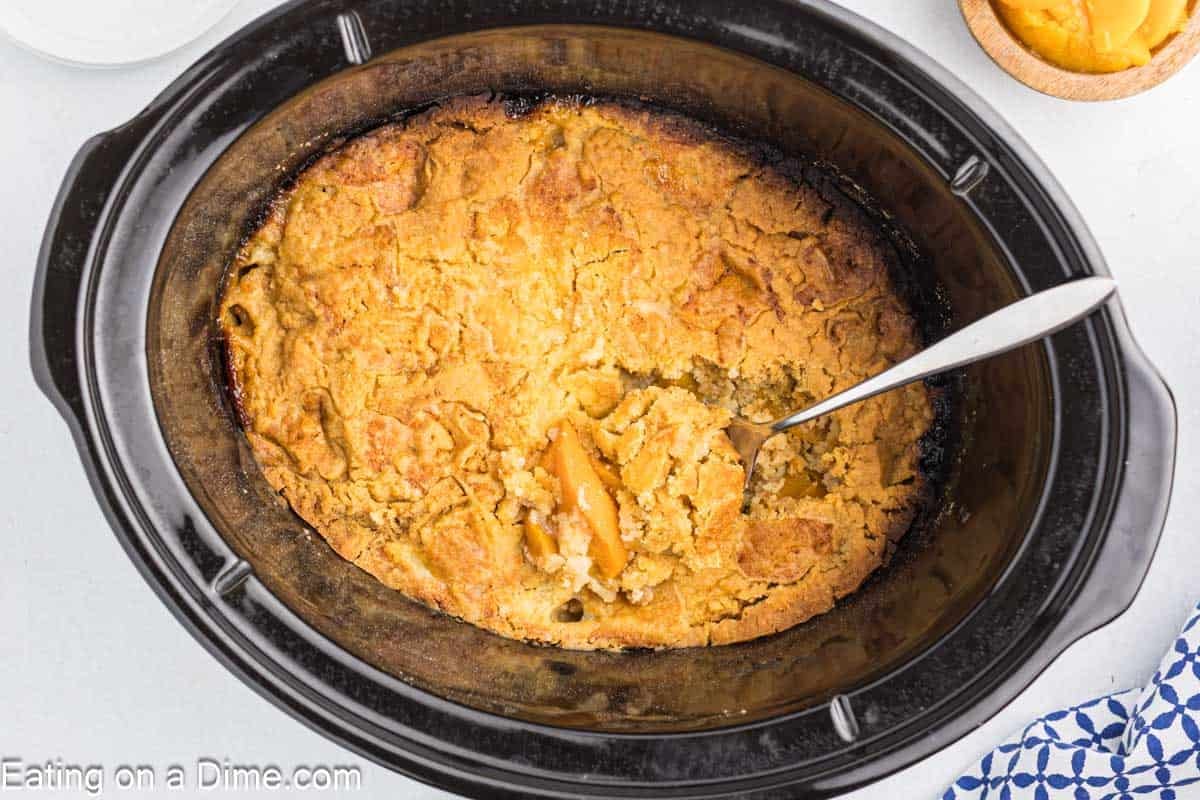 Peach Dump Cake in a slow cooker topped with a golden brown crust with a silver spoon