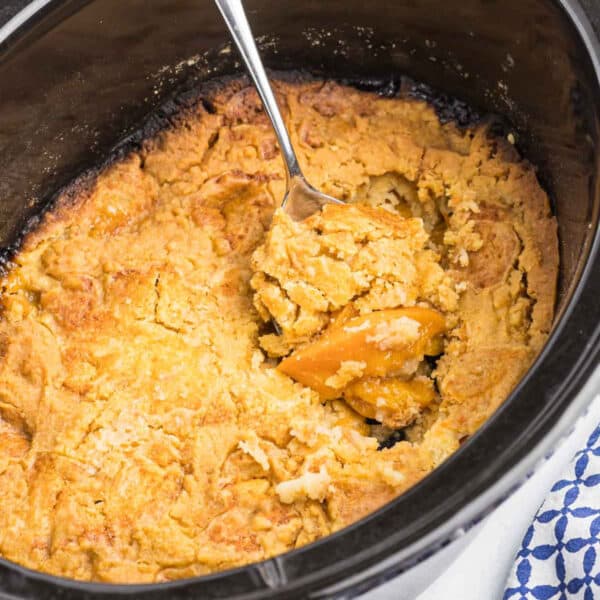 Easy peach dump cake in a slow cooker with a large spoon scooping out a serving.