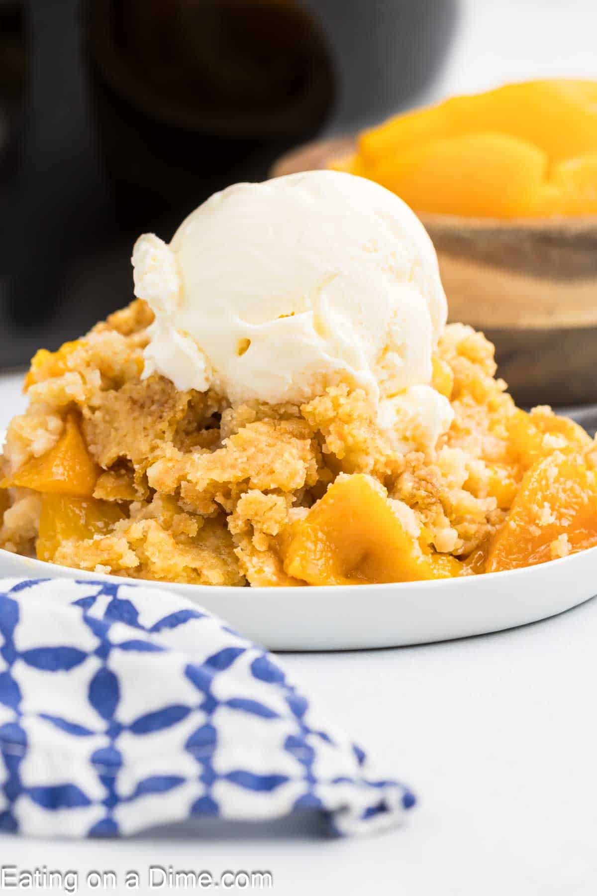 A serving of peach dump cake on a white plate topped with vanilla ice cream