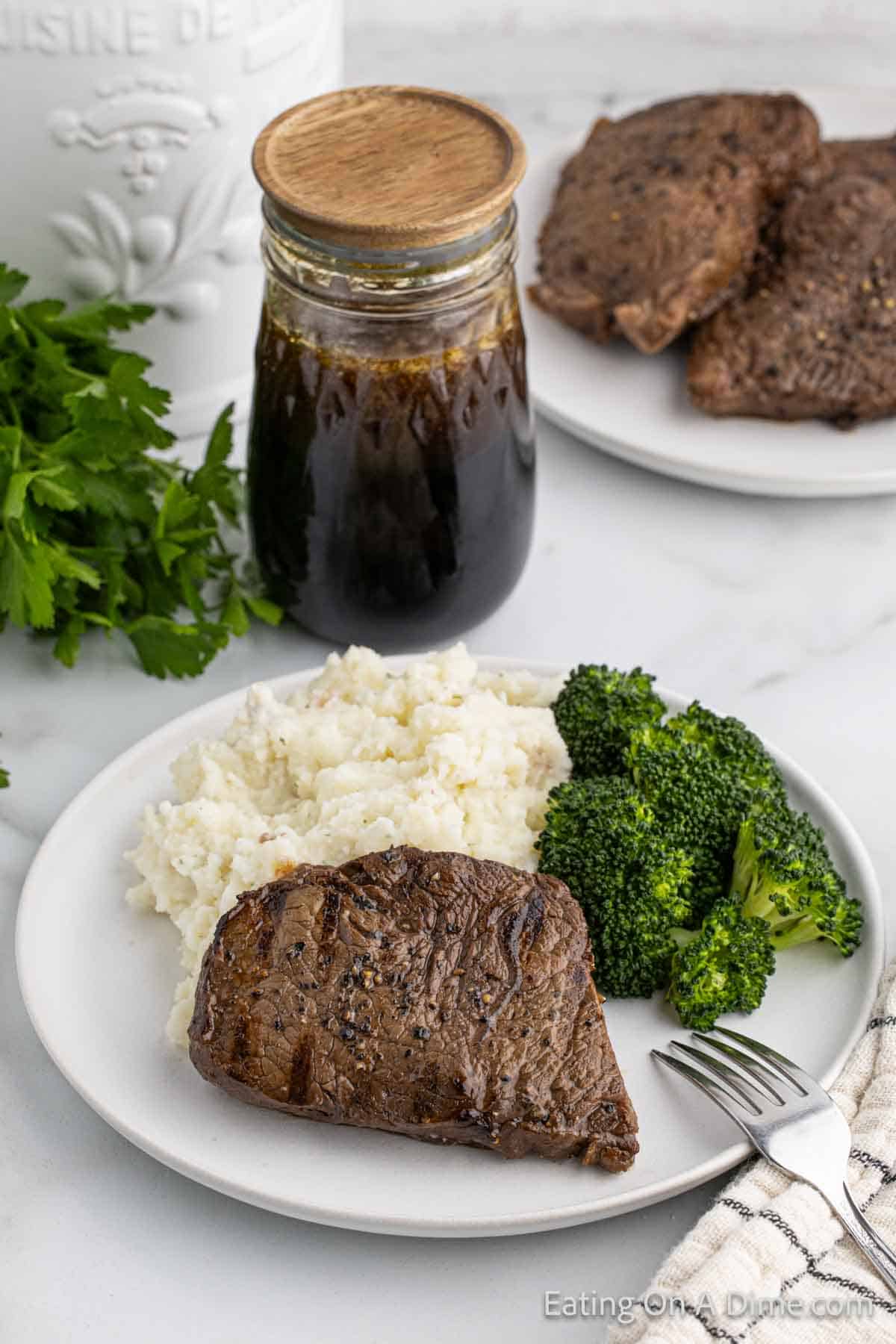 Grilled Steak on a plate with mashed potatoes and broccoli with a jar of marinade on the side