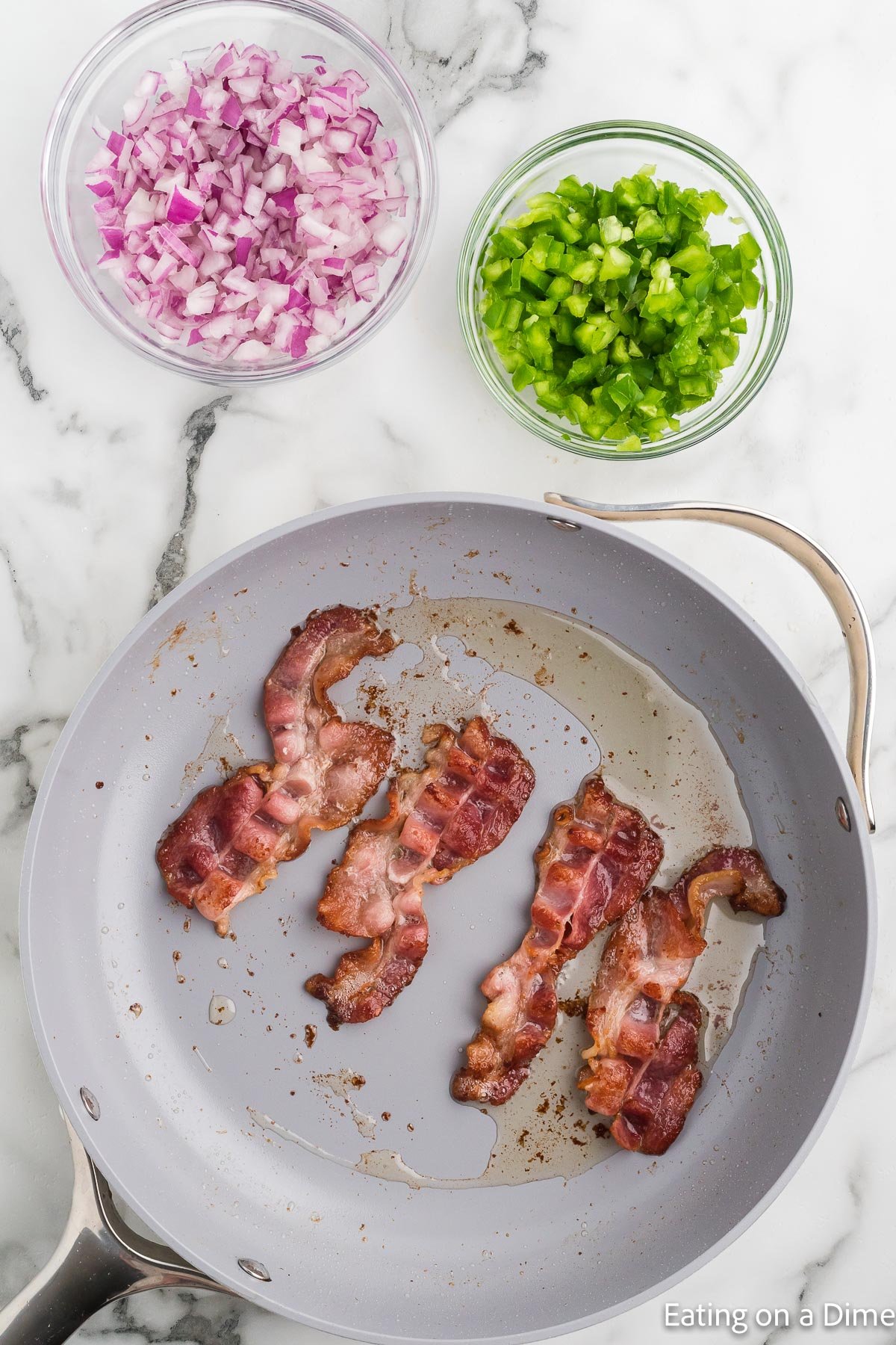 Cooking bacon in a skillet and bowls of red onions and bell peppers