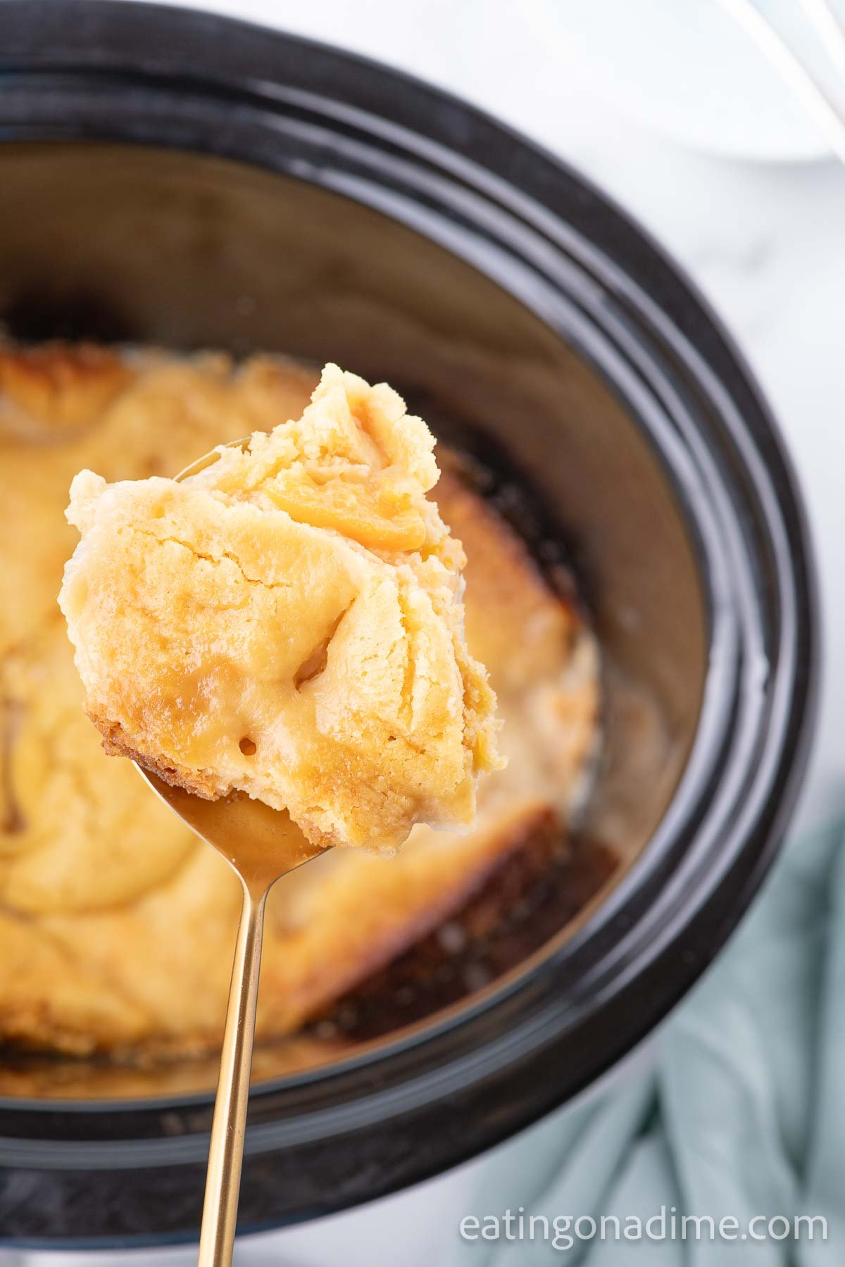Close up image of slow cooker peach dump cake in the crock pot with a serving on a spoon