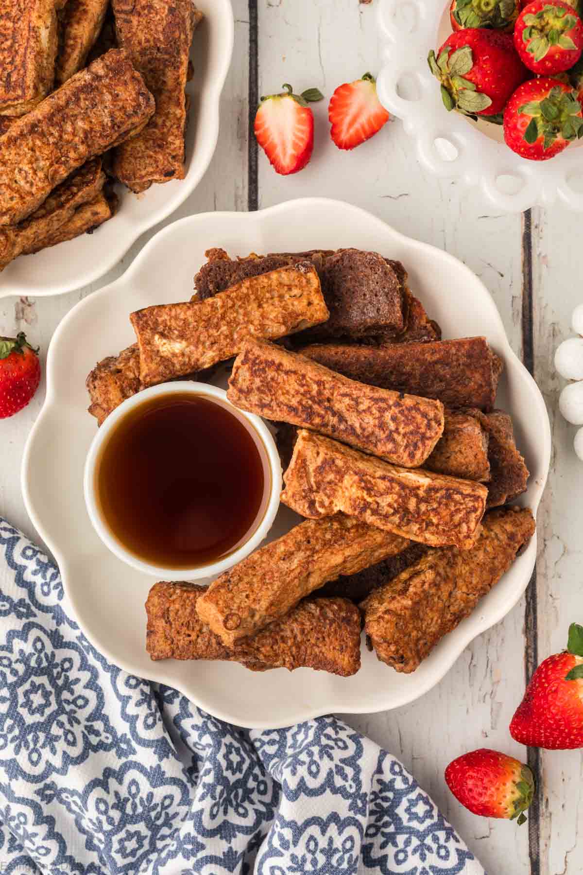 French Toast Sticks stacked on a white platter with a side of syrup in a bowl
