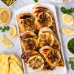 Grilled chicken with lemon wedges on a white platter.