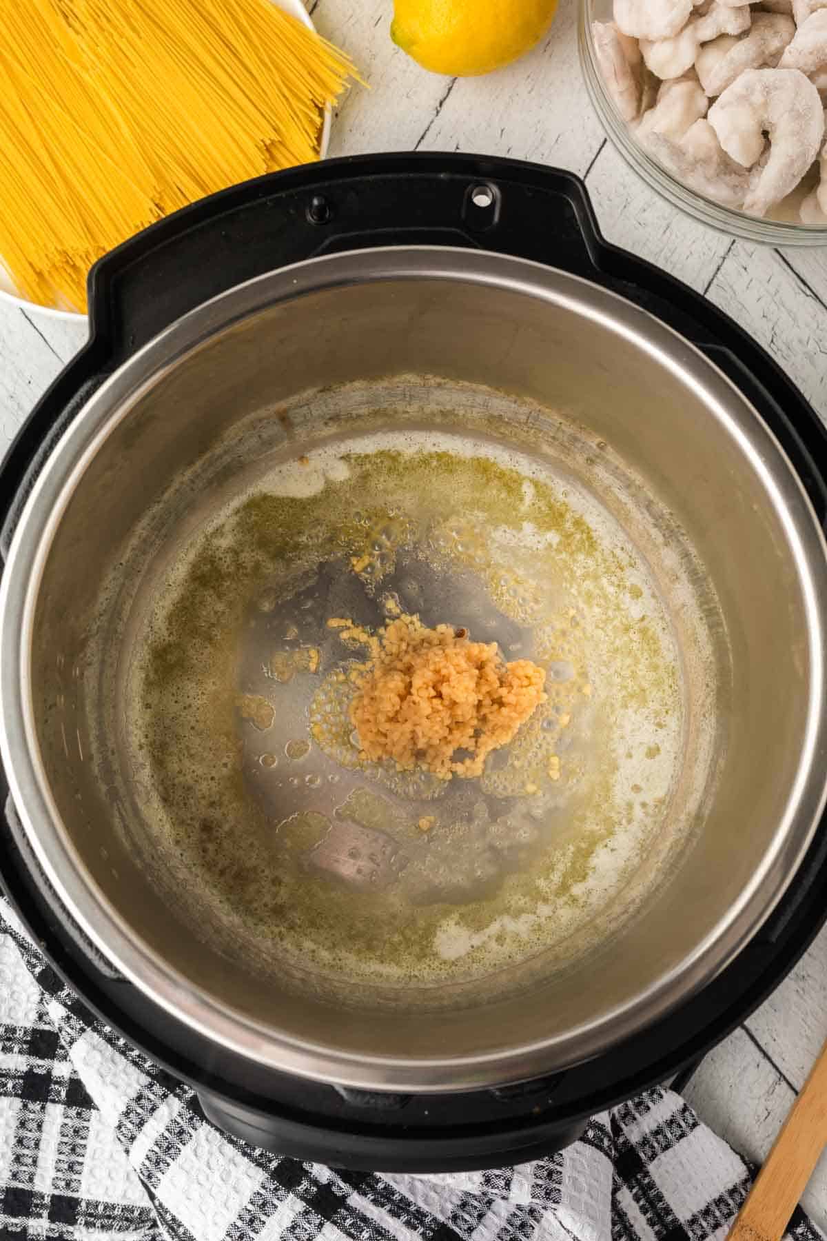 Adding minced garlic to the instant pot with melted butter