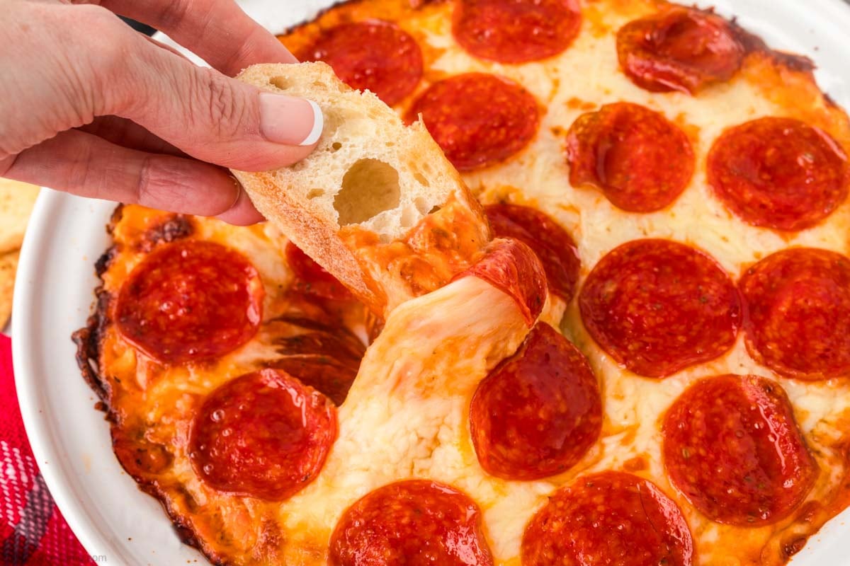 Pepperoni Pizza Dip in a white dish with a piece of French Dip being dipping into it.