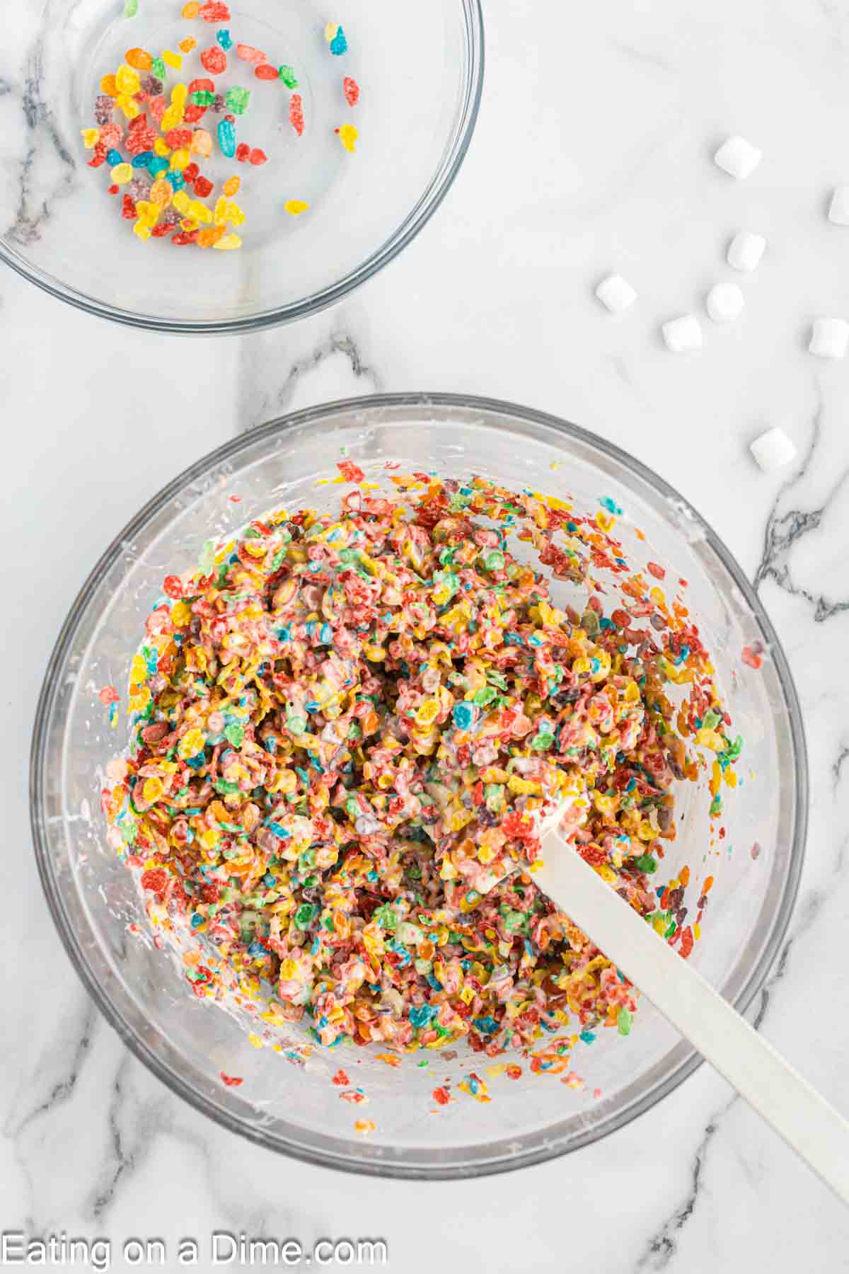 Combining the melted marshmallow mixture with the cereal in a bowl with a spatula