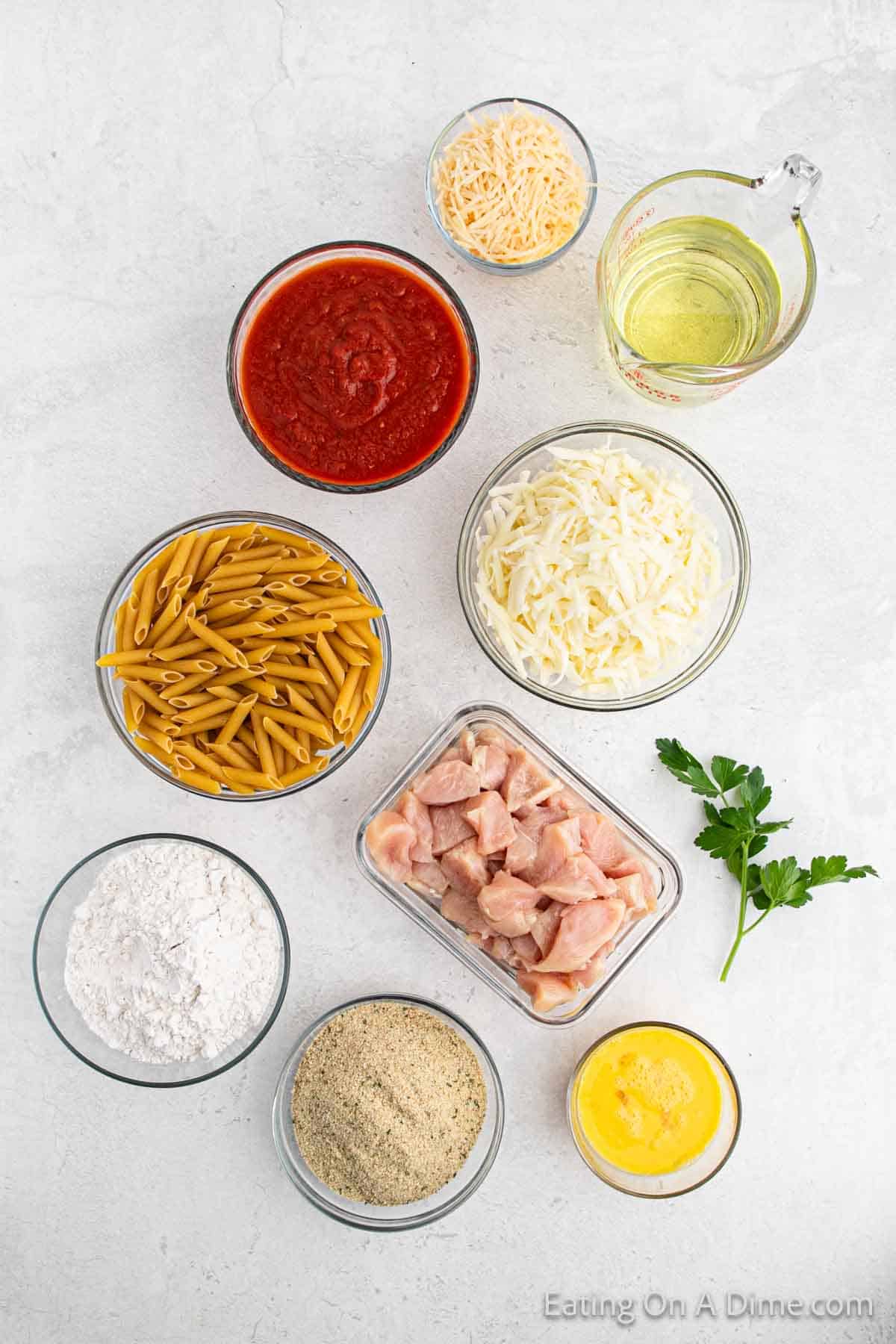 Chicken parmesan pasta ingredients - vegetable oil, chicken breasts, flour, eggs, bread crumbs, penne pasta, marinara sauce, mozzarella cheese, parmesan cheese, parsley