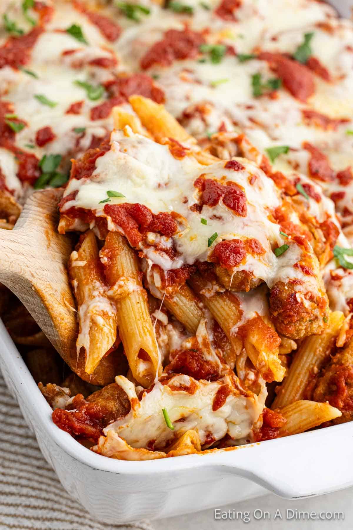 Chicken Parmesan Casserole in a baking dish topped with melted cheese with a serving on the wooden spoon