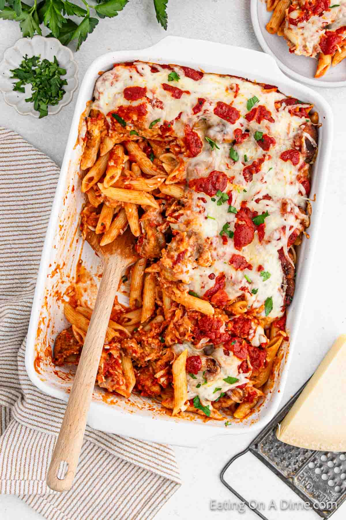 Close up image chicken parmesan pasta in a baking dish with a wooden spoon