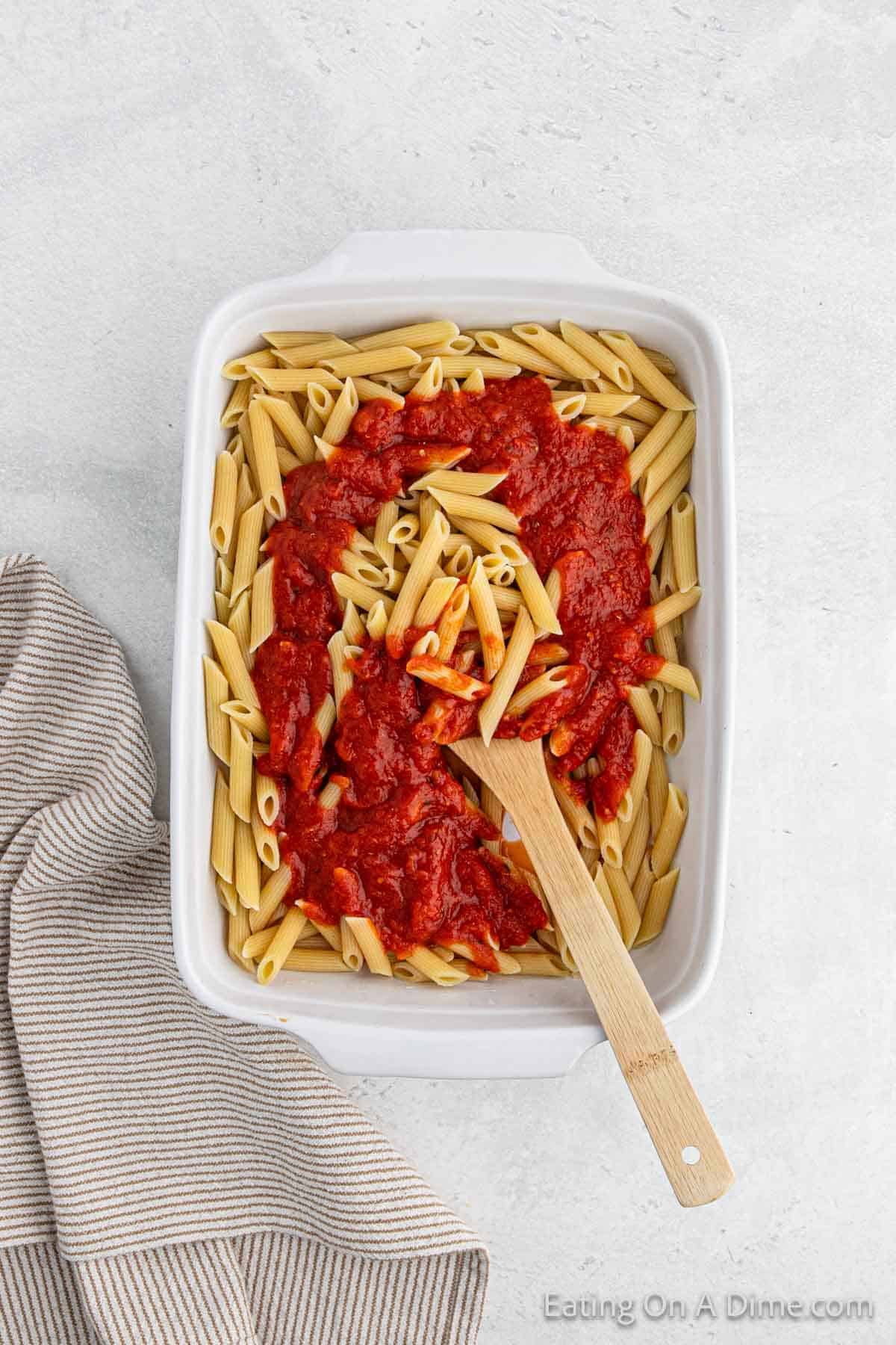 Placing the cook pasta in a baking dish and topping with sauce with a wooden spoon