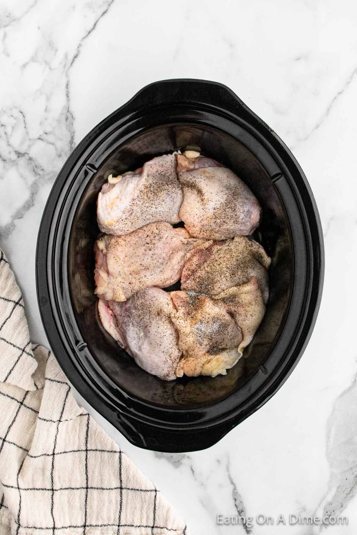 Placing chicken thighs in the slow cooker topped with salt and pepper