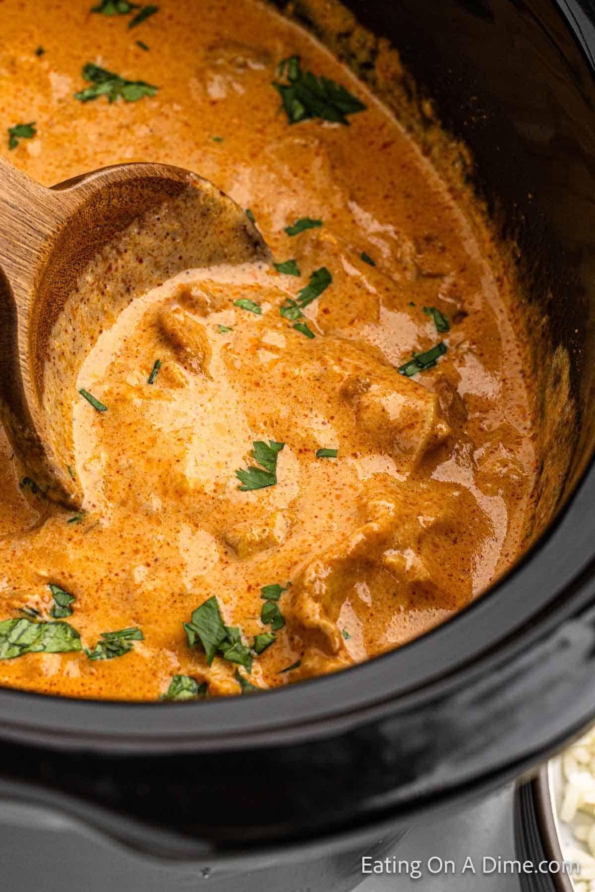 Close up image of butter chicken in a slow cooker with a wooden spoon