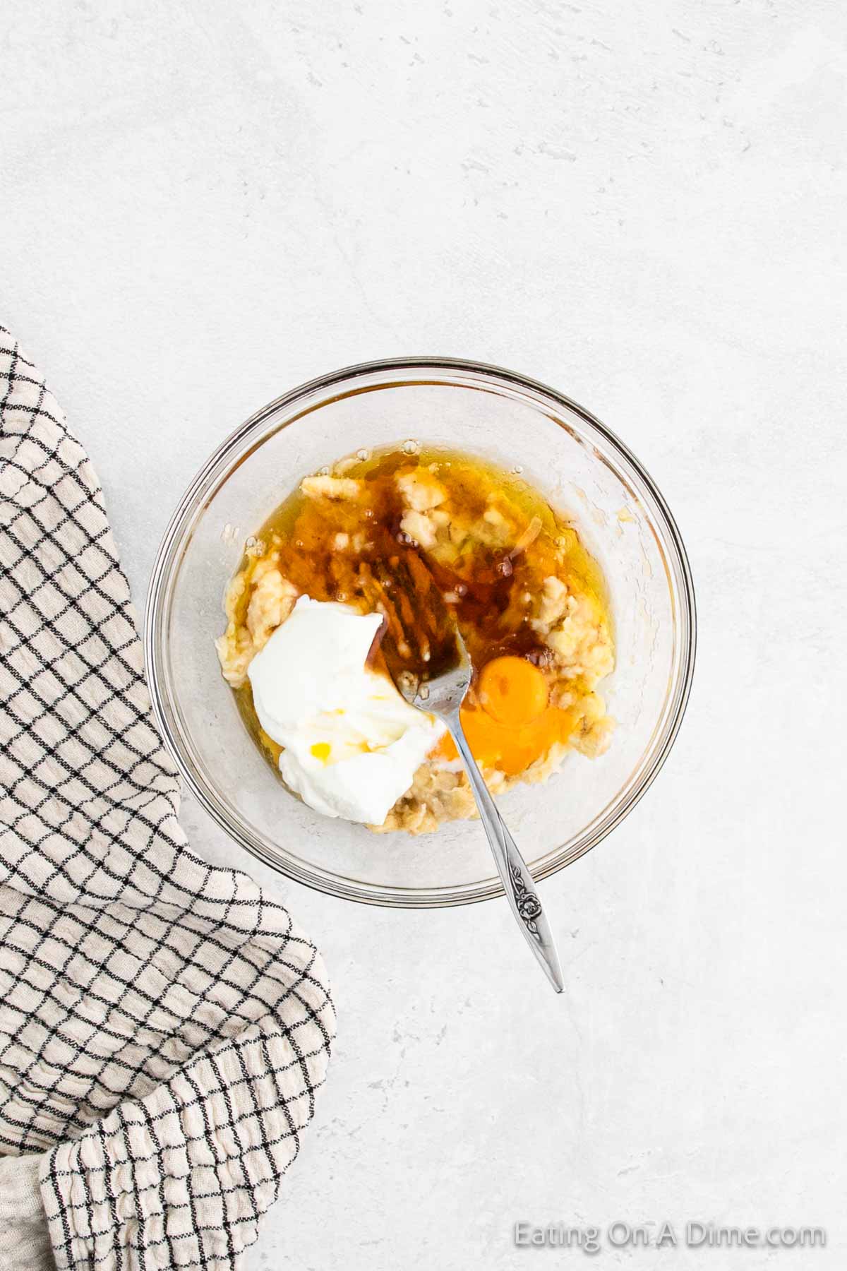 Combining egg, maple syrup, Greek Yogurt, vanilla, and melted butter in a bowl with a fork