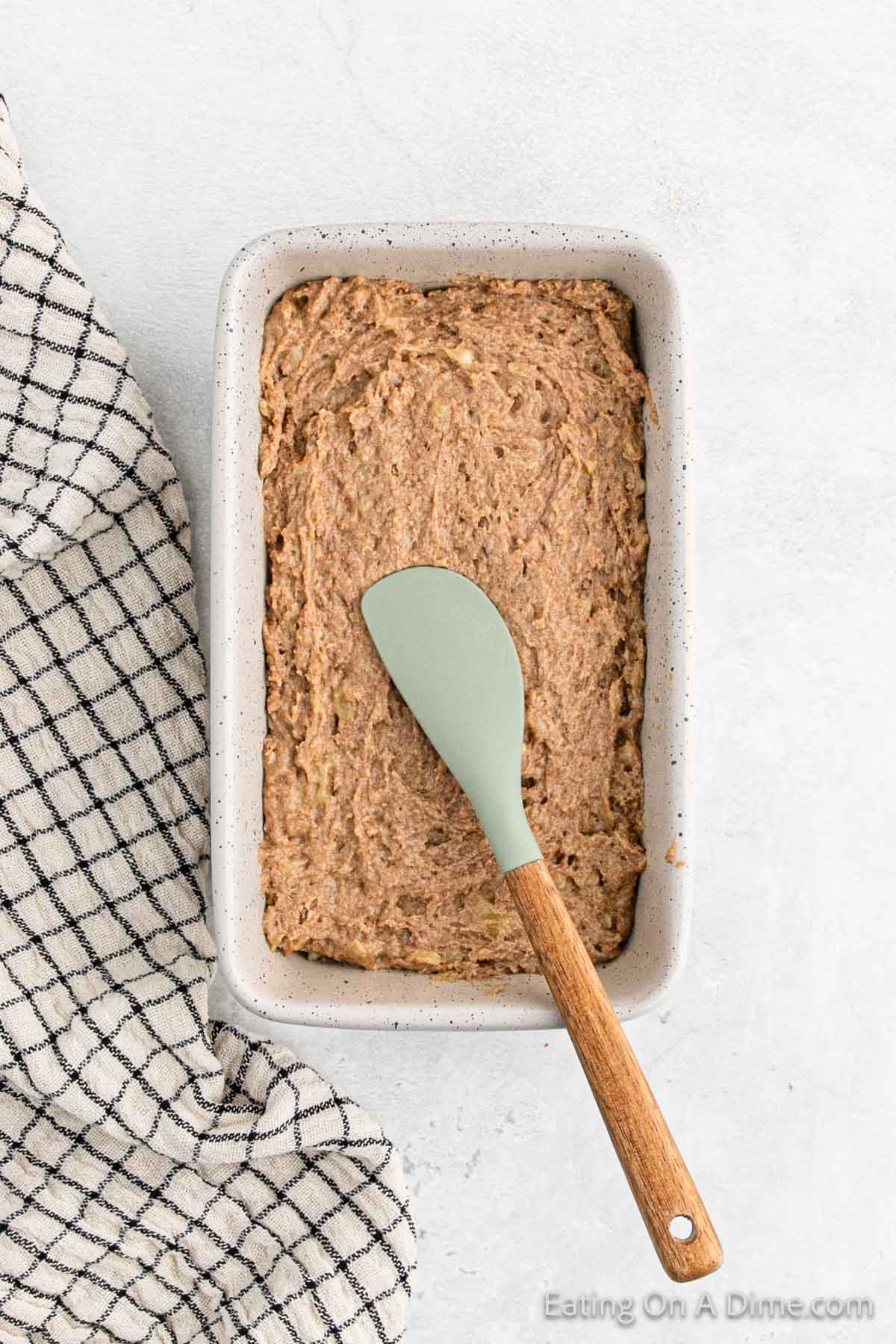 Spreading banana bread batter in a loaf pan with a spatula