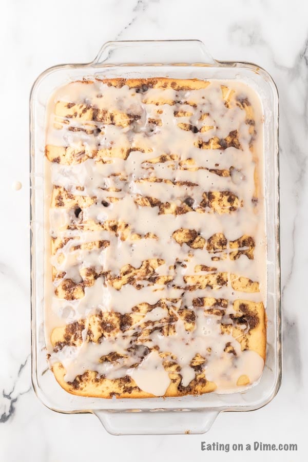 Overview of the cinnamon roll cake in a glass pan with the glaze drizzled on top of it. 
