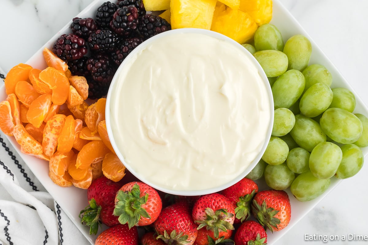 It doesn't get much easier than this 2 ingredient fruit dip recipe! It's so easy the kids can make it after a long day in the pool! Fruit dip on a platter with a side of grapes, strawberries, small oranges, blackberries and pineapple