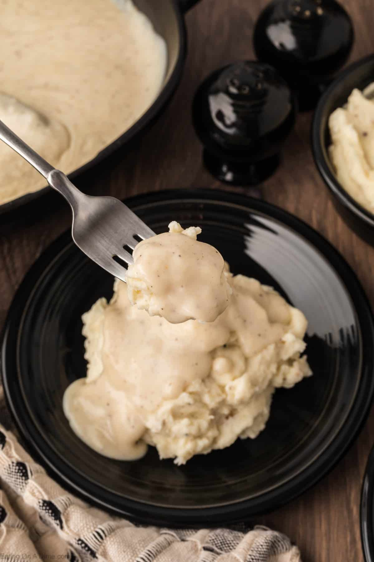 White Gravy topped mashed potatoes on a black pepper with a bite on a fork