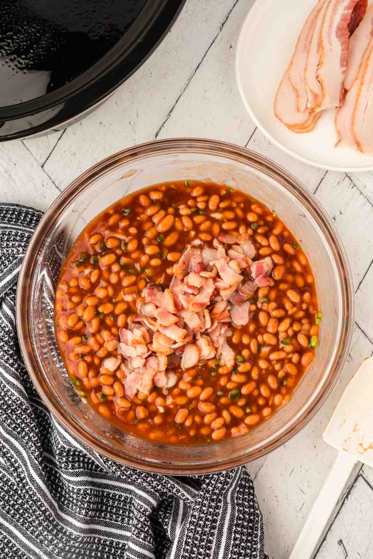 Adding in the chopped bacon into the pork and beans mixture in the bowl