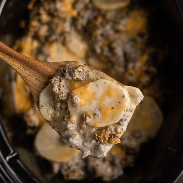 Close up image of crock pot hamburger potato casserole with a serving on a wooden spoon. 
