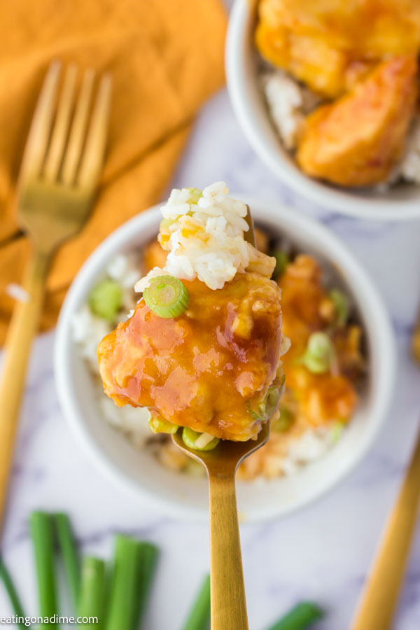 Close up image of orange chicken in a bowl with rice with a serving on a fork. 