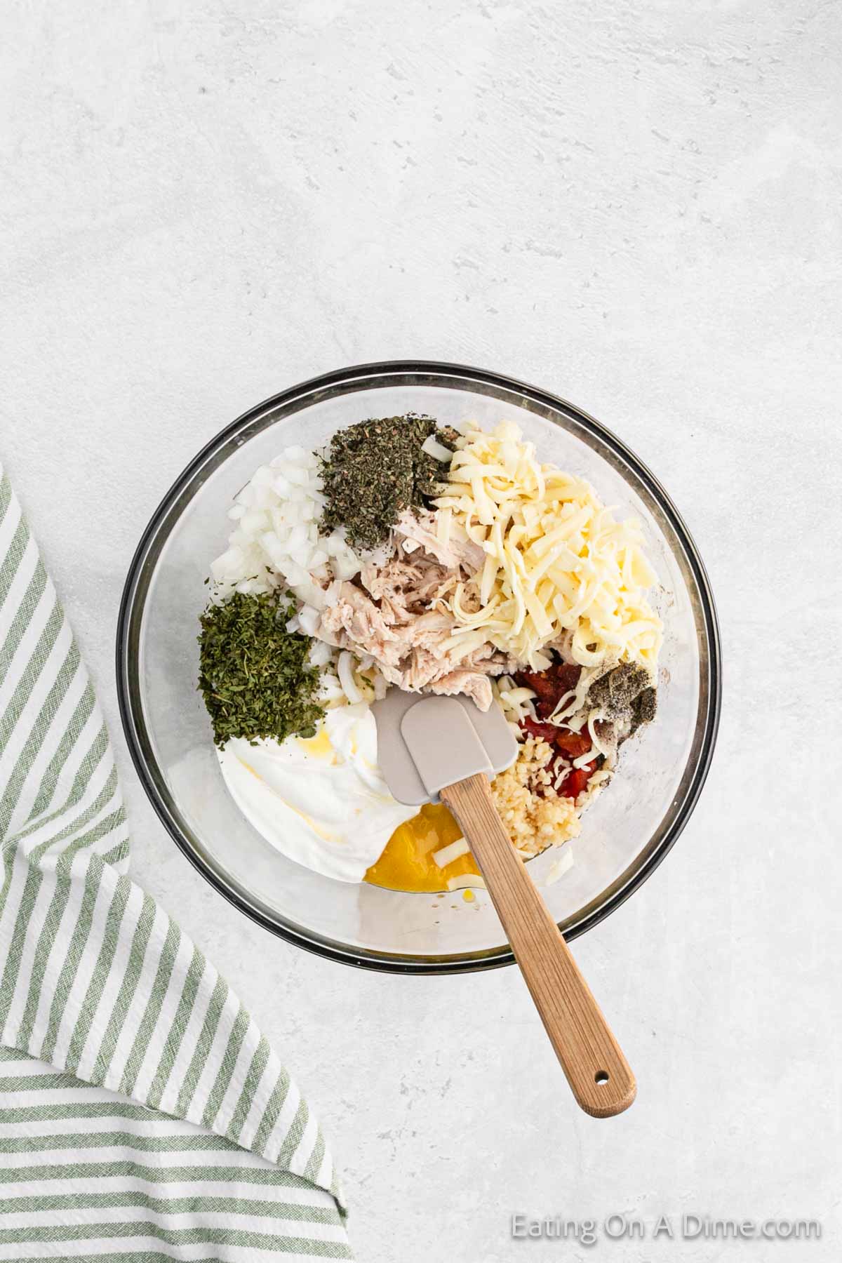 Mixing shredded chicken, soups, seasoning, and fresh vegetables in a bowl with a spatula
