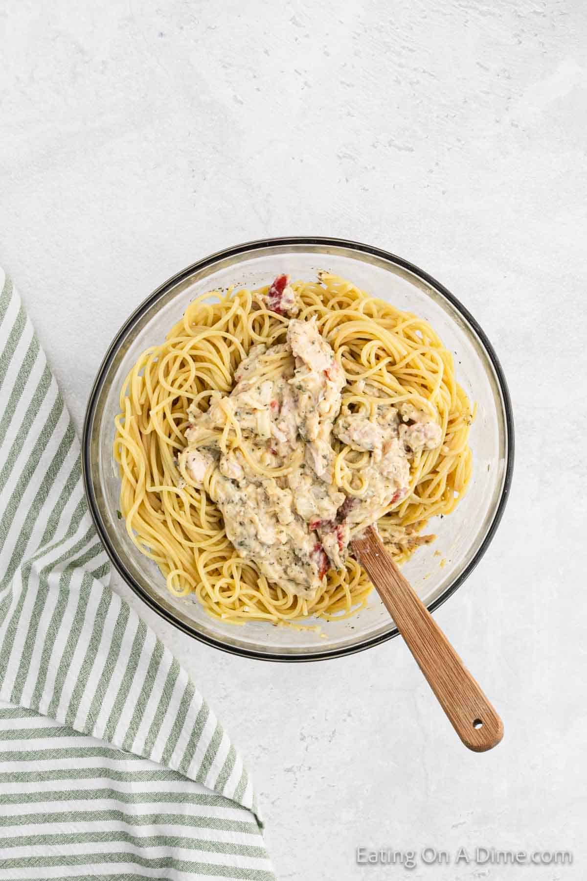 Combining the chicken mixture with the cooked spaghetti noodles in a bowl with a spatula