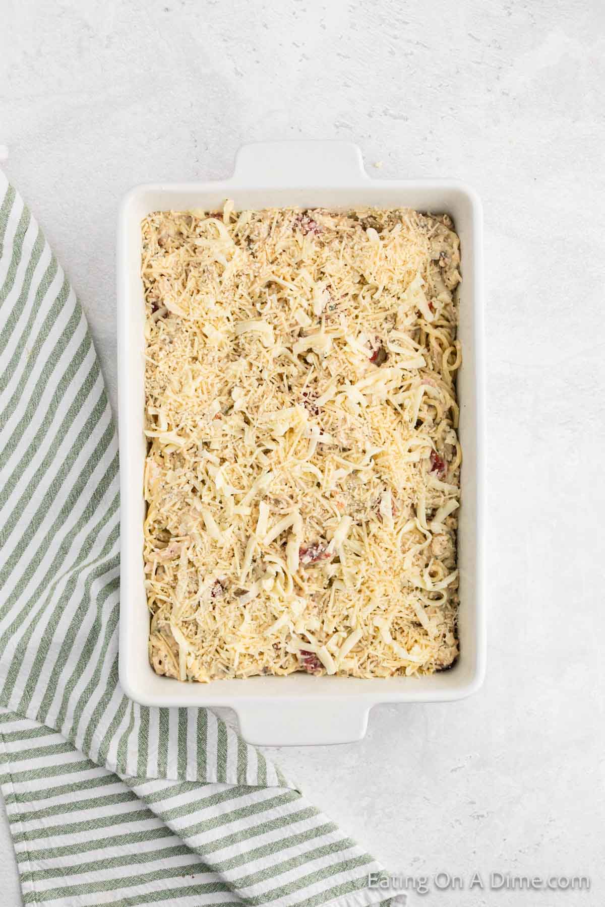 Topping the chicken spaghetti casserole in baking dish topped with shredded cheese and parmesan cheese