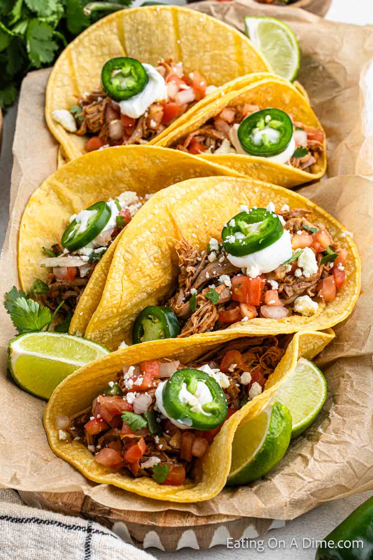 Shredded pork tenderloin tacos placed in a serving platter. The tacos are topped with pico de gallo, slice jalapenos and sour cream 