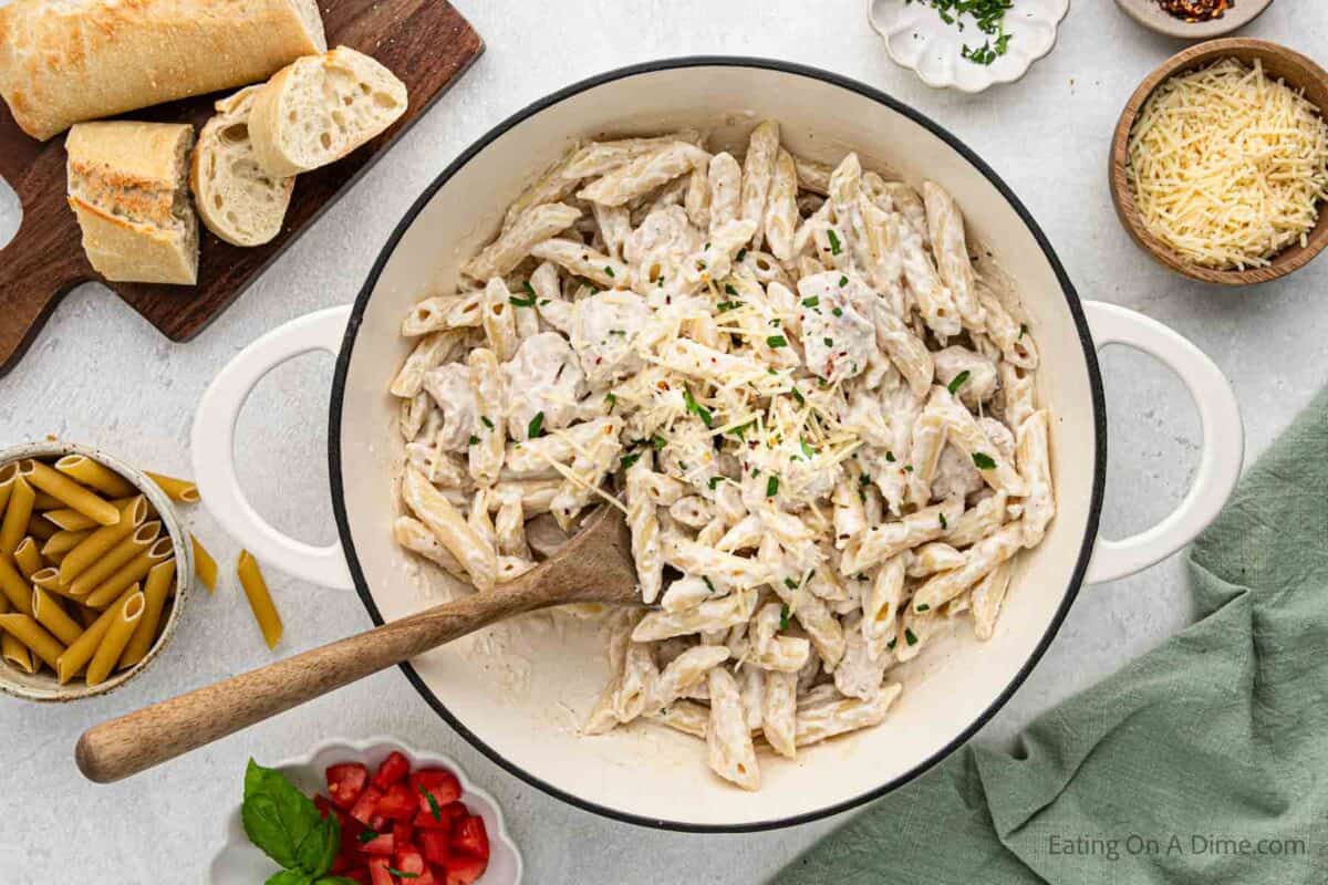 Chicken penne pasta in a large skillet with a wooden spoon