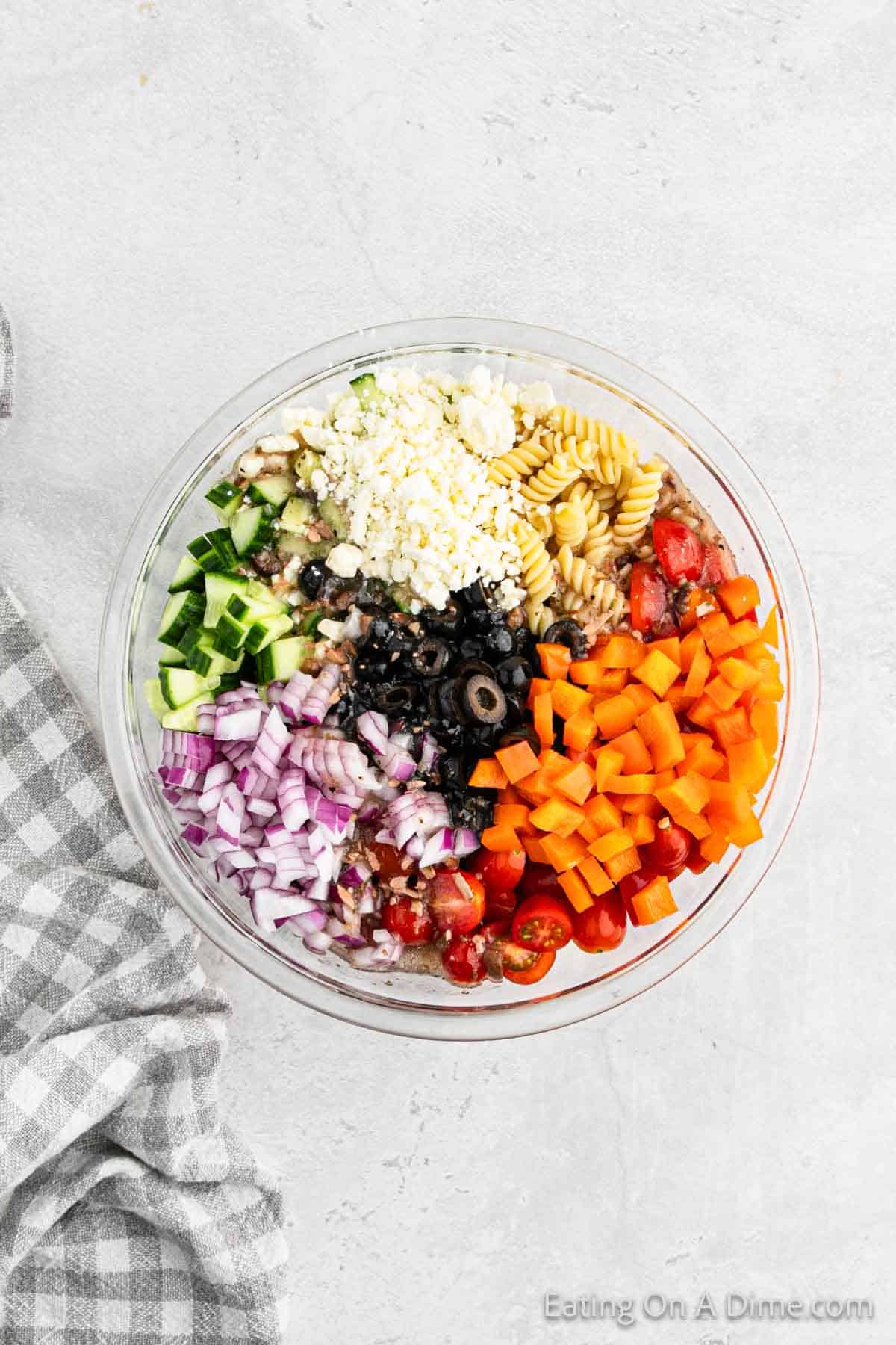 Cooked pasta in a bowl with feta cheese, orange bell pepper, cherry tomatoes, red onions, cucumber