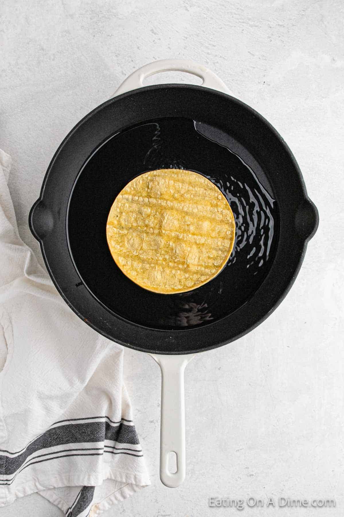 Placing corn tortillas in hot oil in a cast iron skillet
