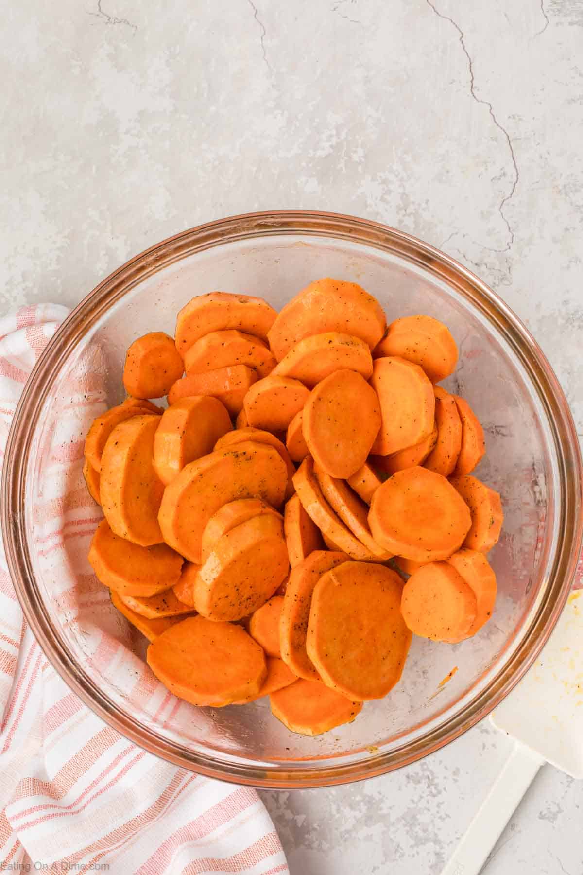 Sliced sweet potatoes in a bowl seasoned with oil and salt and pepper