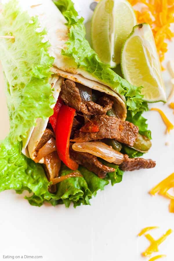 A beef fajita wrapped in a tortilla and lettuce with limes next to it 
