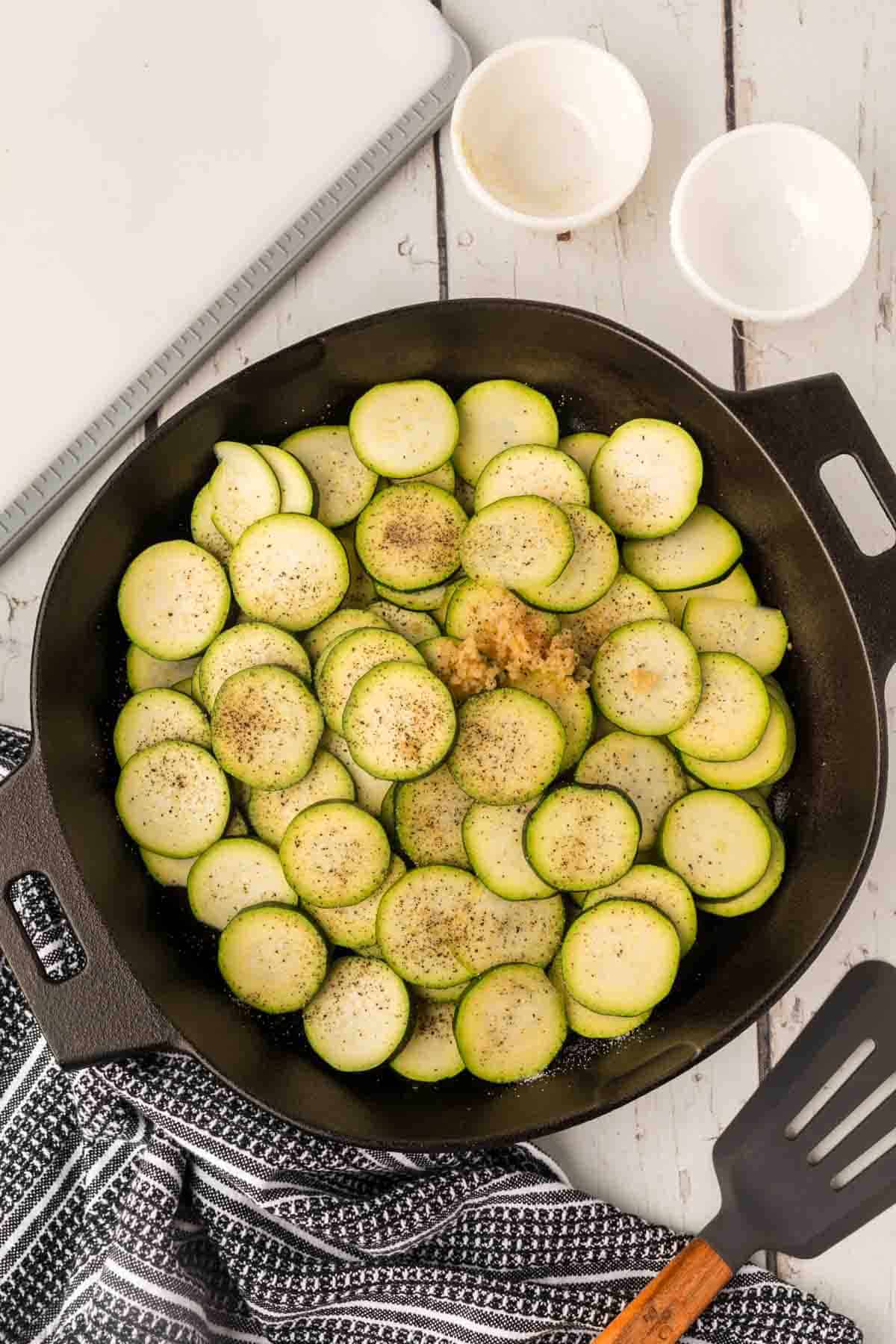 Slice zucchini in a cast iron skillet topped with minced garlic and seasoning