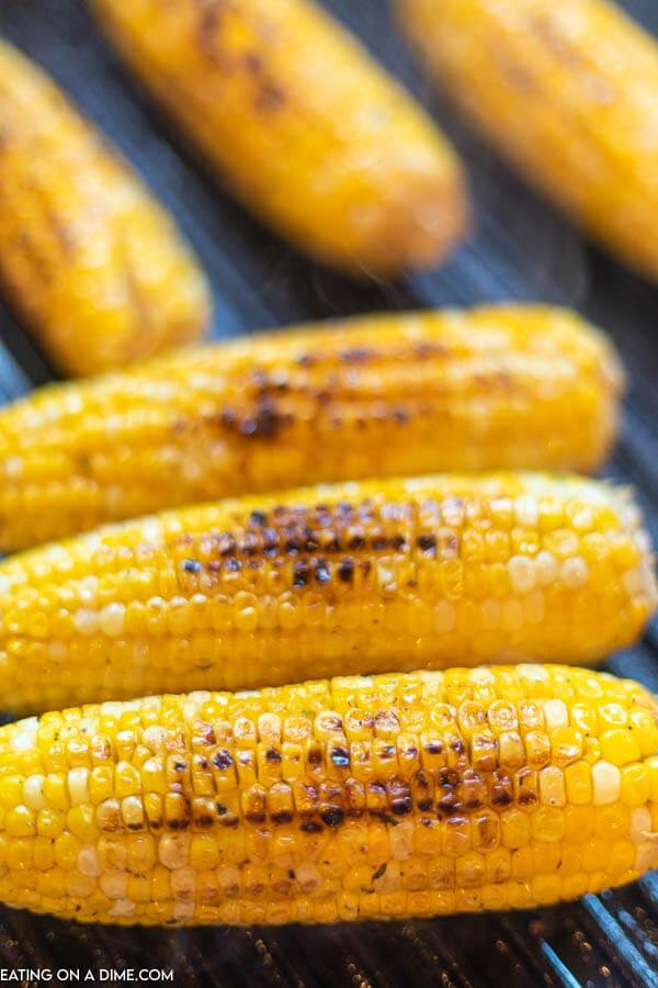 3 corn on the cobs that have been grilled directly on the grill grates and have some charring marks on the corn. 