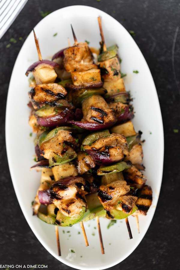 5 chicken kabobs on a white platter on a black countertop. 