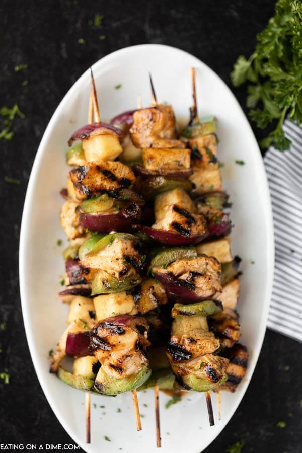 Grilled Hawaiian Chicken Kabobs on a white platter with a striped linen in the back ground. 