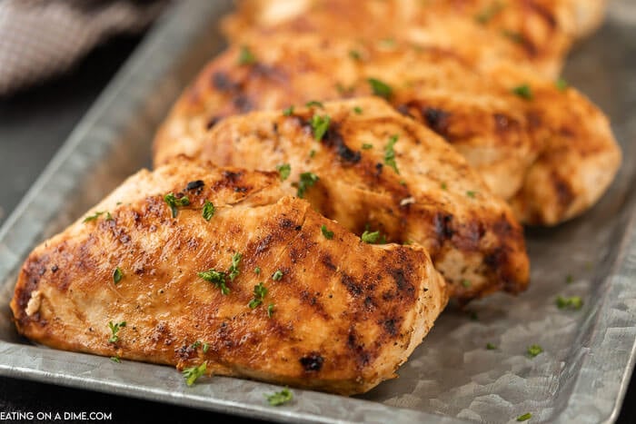 Close up of grilled chicken breasts on a silver platter topped with fresh parsley. 