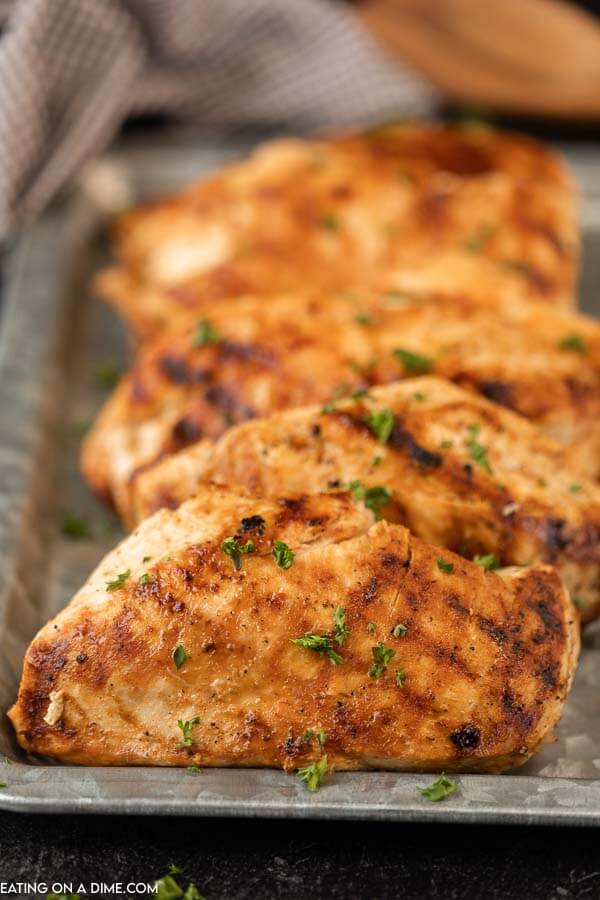 Multiple grilled chicken breasts on a silver platter. 