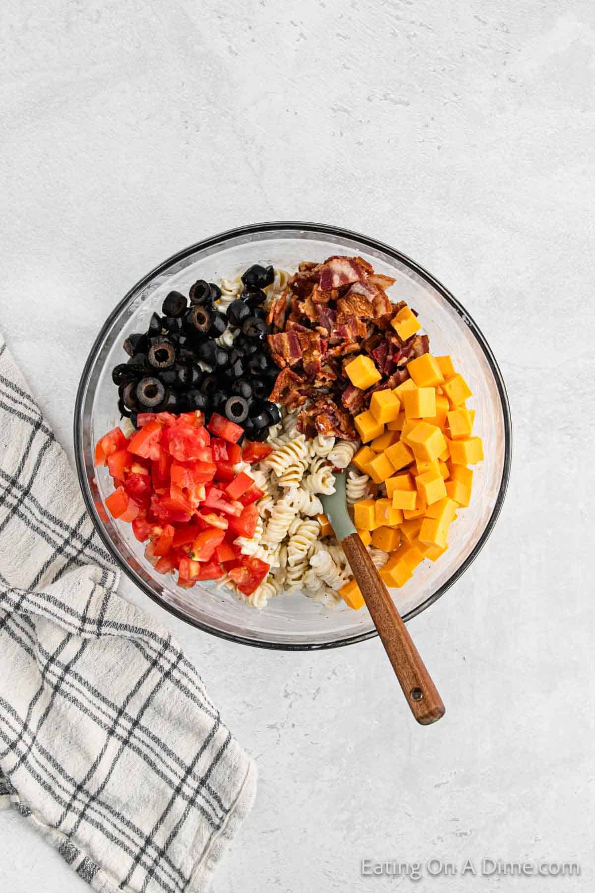 Black olives, chopped bacon, cheese cubes, pasta, diced tomatoes in a bowl with a spoon